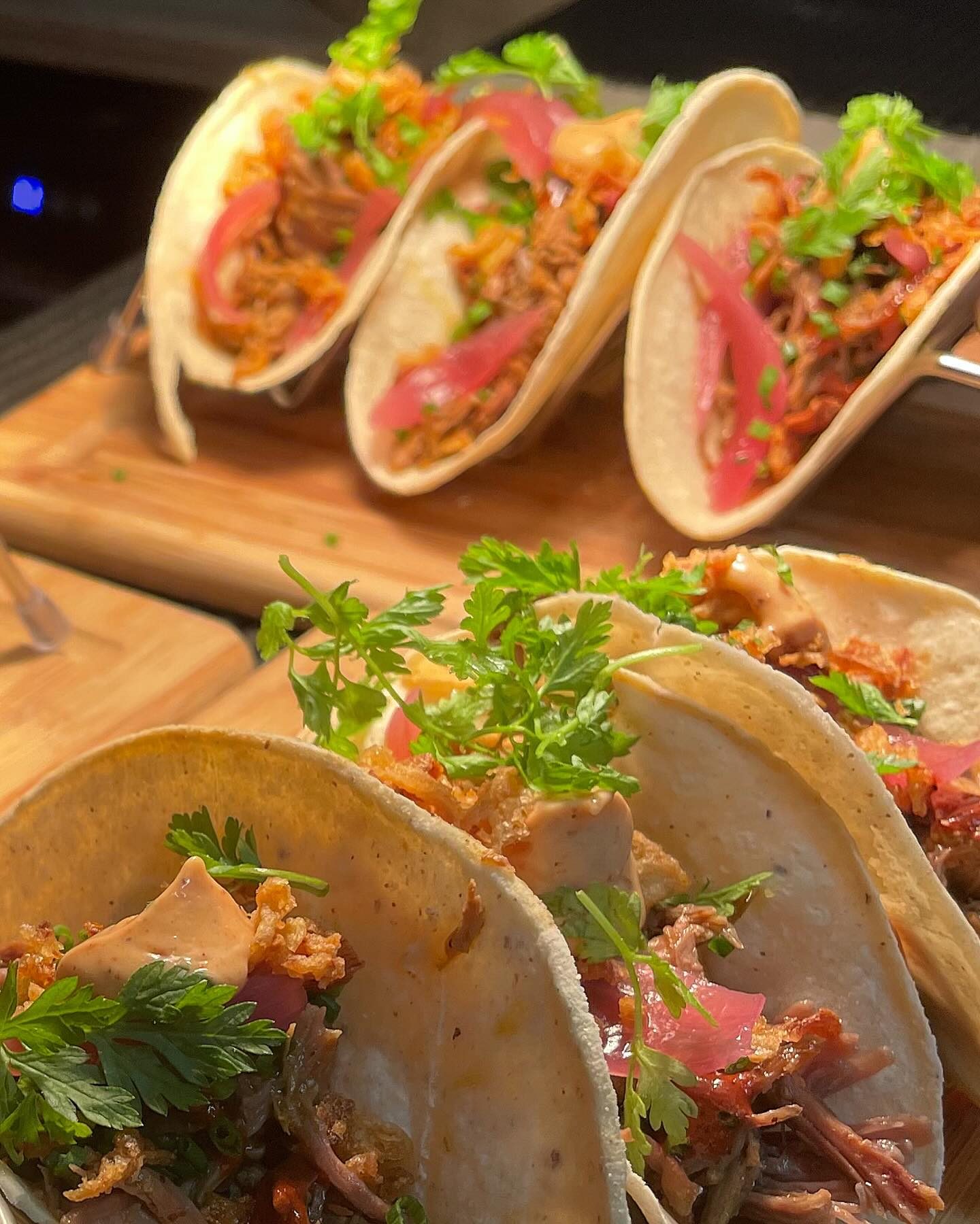 Des tacos garnis de viande effilochée et d'herbes, sur une planche